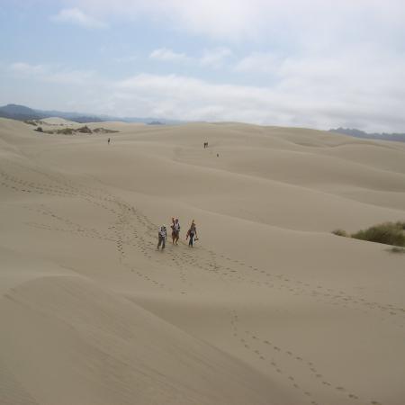 Three individuals walking through sand dunes, leaving footprints in their wake.